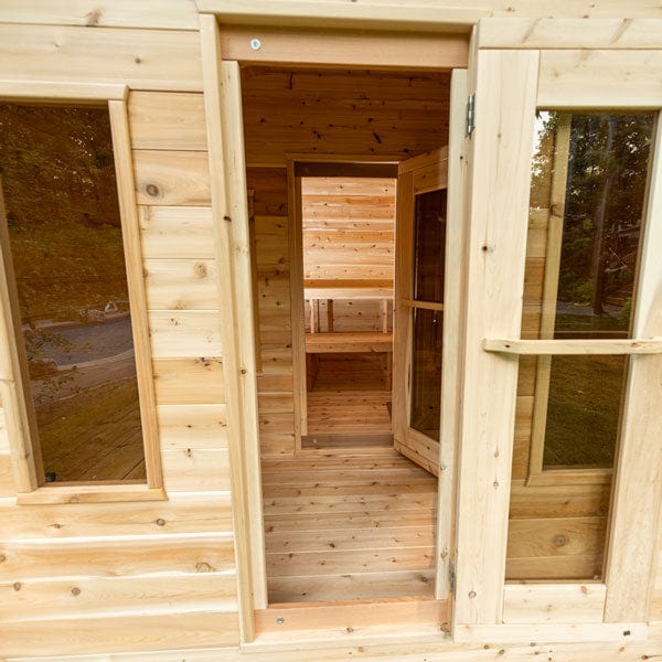Wooden sauna with open door, showing interior benches and windows.